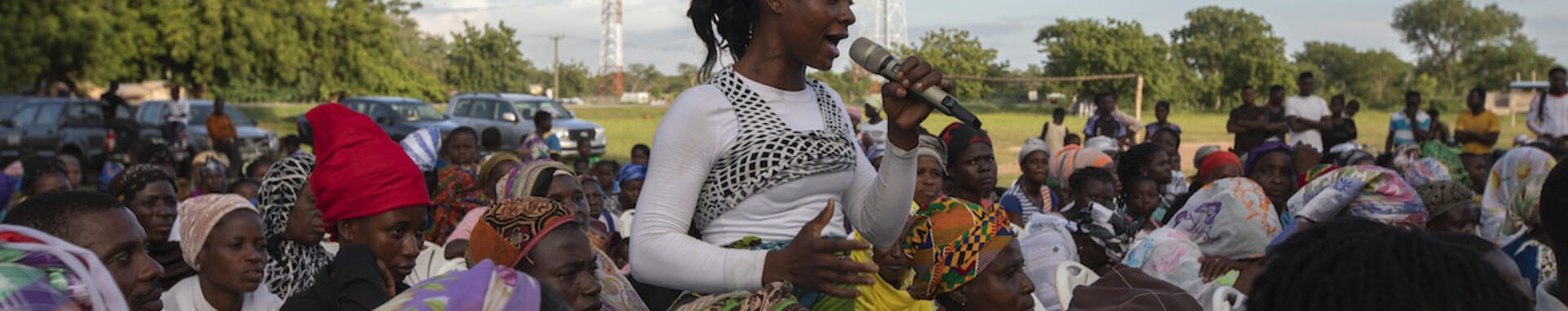 A young African woman is up on someone's shoulder in a demonstration and talking in a microphone