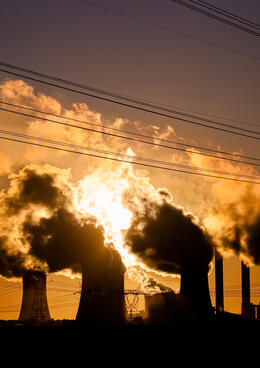 A coal power plant emits smoke against a sunset