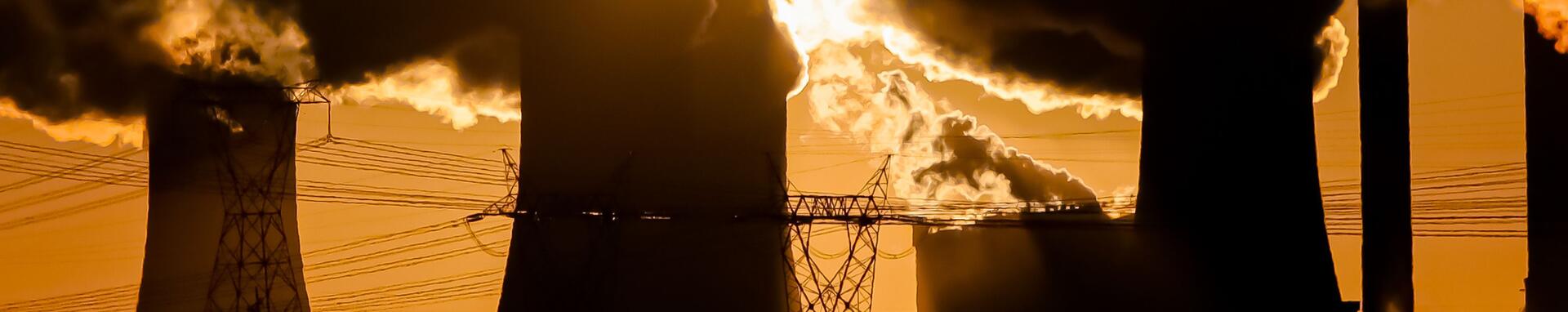 Coal power plant emits smoke against an orange sunset